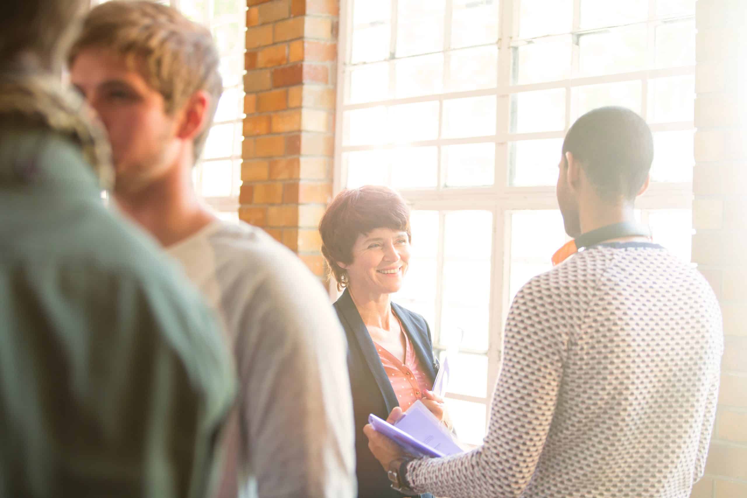A small group of people talk together in a sunlit community room.