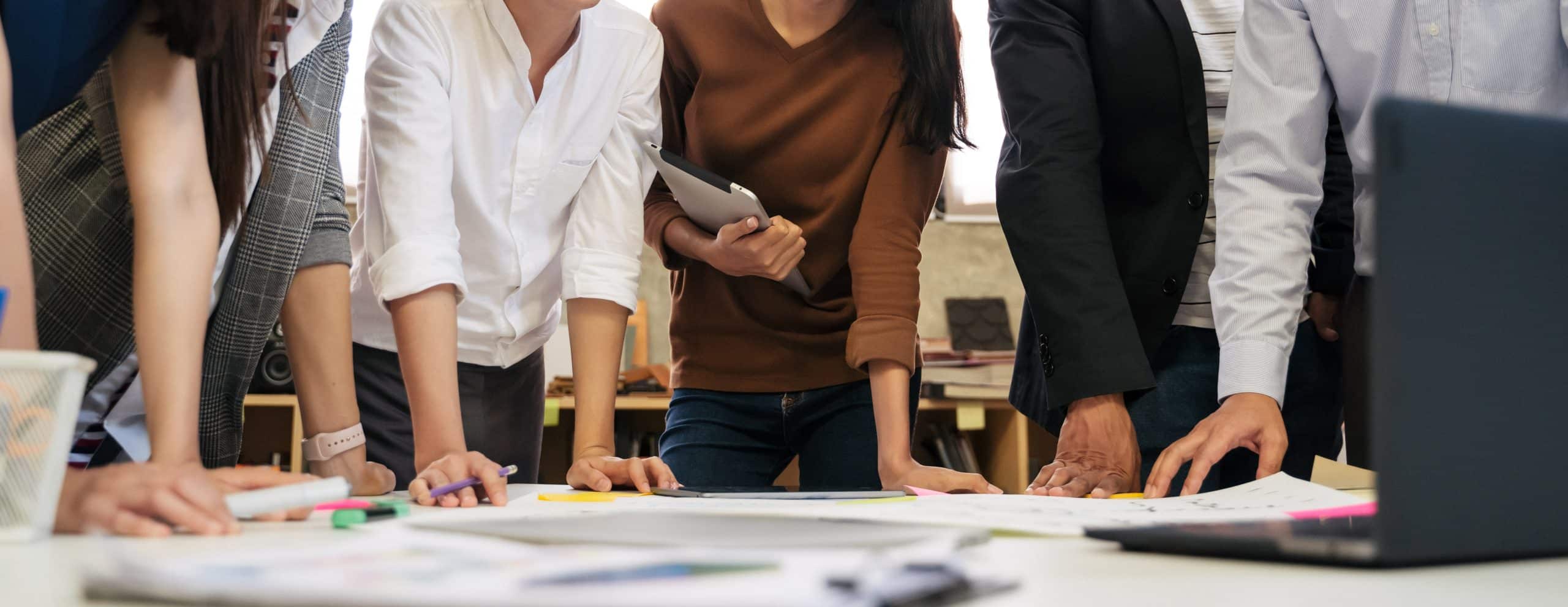 A group of people leaning over a table covered with plans and a laptop